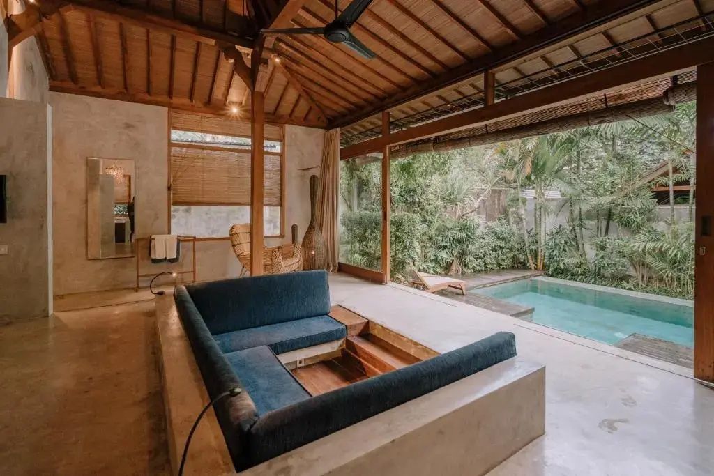 Blick aus dem Wohnzimmer mit vertiefter Couch auf den eigenen Pool und tropische Pflanzen.