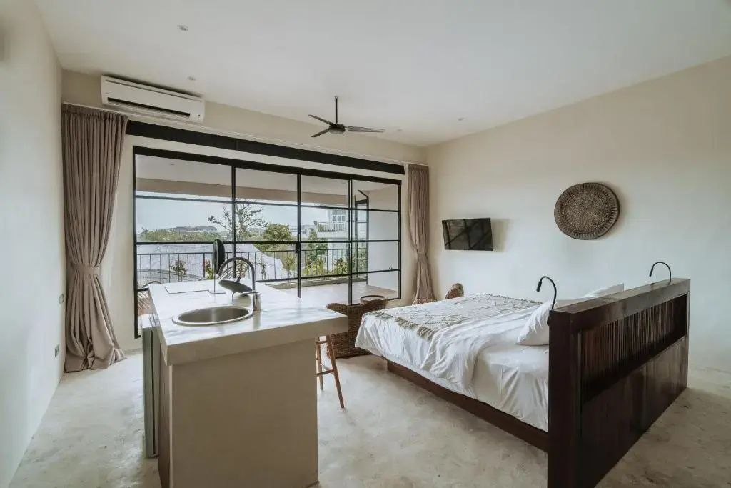 Hotelzimmer mit Kochinsel, Doppelbett und großen Glasschiebetüren zum Balkon.