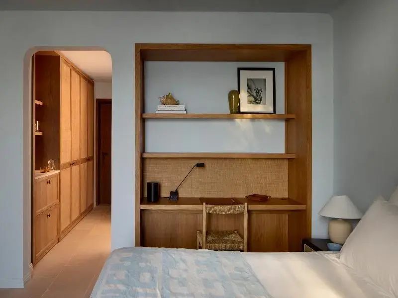 Ein eingerichtetes Schlafzimmer mit eingebautem Schreibtisch aus Holz und Bett im Vordergrund.