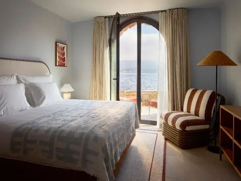 Hell eingerichtetes Schlafzimmer mit Doppelbett und Blick durch die Balkontür auf das Meer.