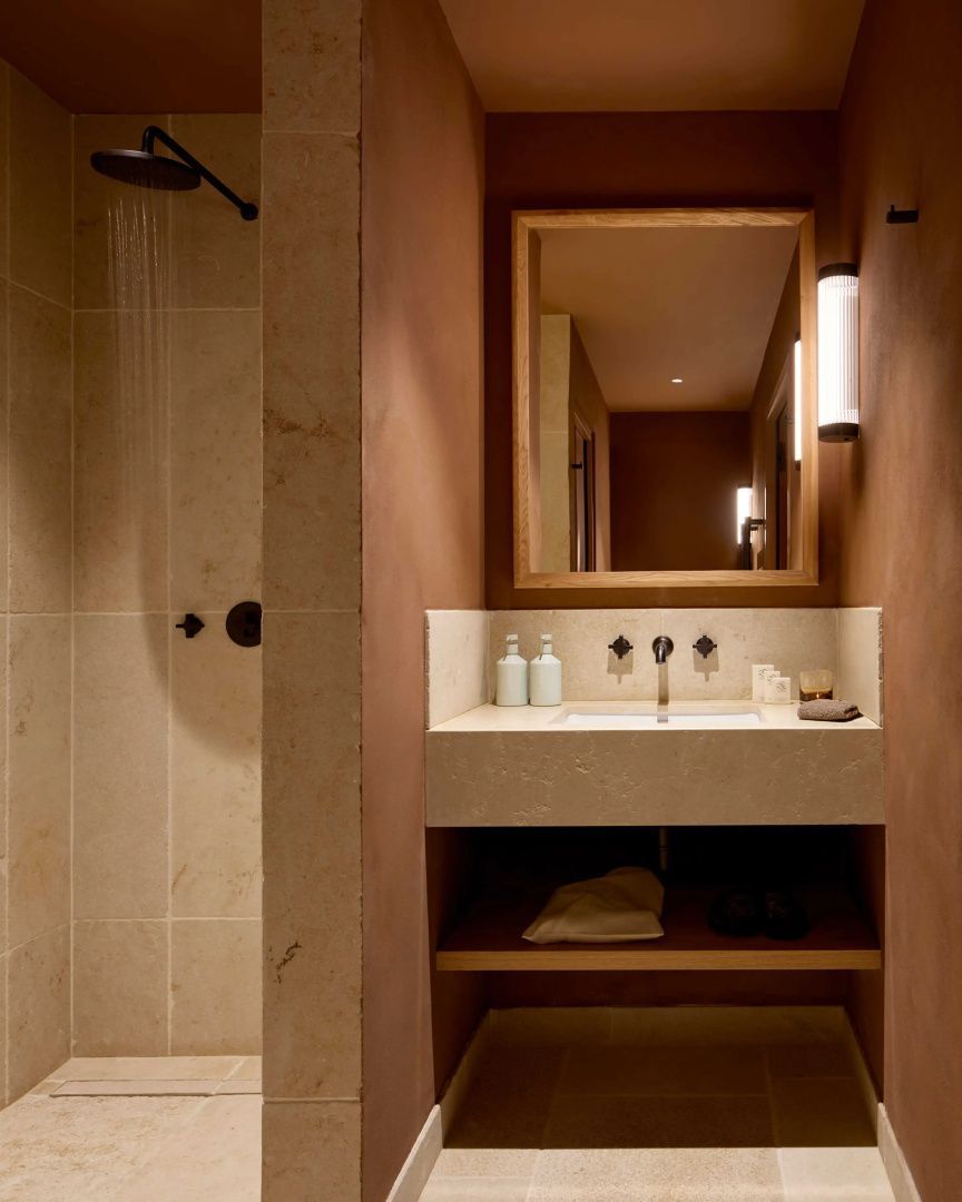 Badezimmer mit Regendusche aus Naturstein und Waschtisch unter einem rechteckigen Holzspiegel.