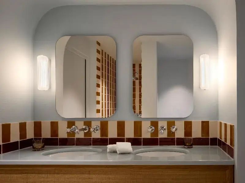 Waschtisch im Badezimmer mit zwei Waschbecken, rechteckigen Spiegeln und Wandleuchten.