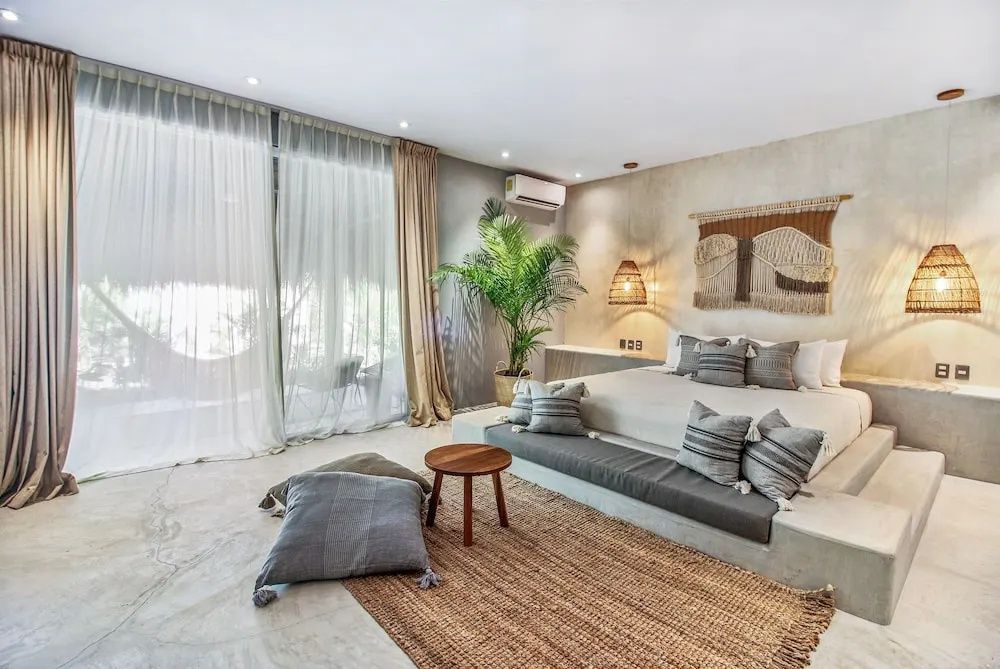 Helles Hotelzimmer mit Doppelbett, Zimmerpflanze, Teppich und bodentiefem Fenster.