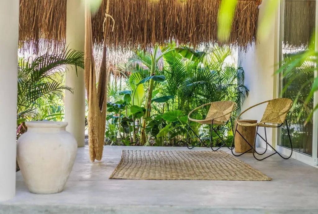 Überdachte Terrasse mit Strohdach, Flechtstühlen, einer Hängematte und grünen Pflanzen im Garten.