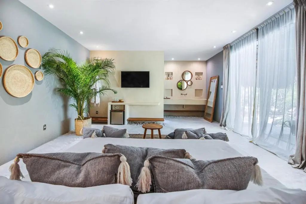 Blick vom Bett auf den Raum mit Fernseher, Zimmerpflanze und offenem Badezimmerbereich.