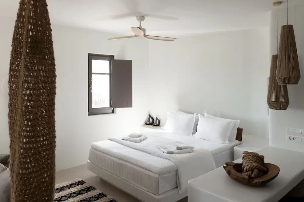 Schlafzimmer in Weiß mit bezogenem Doppelbett, einem Fenster und Holzventilator an der Decke.