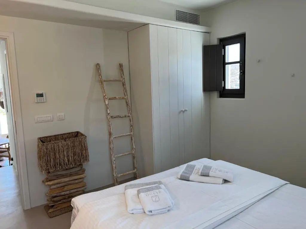 Schlafbereich mit weißem Bett, Holzelementen und Einbauschrank.