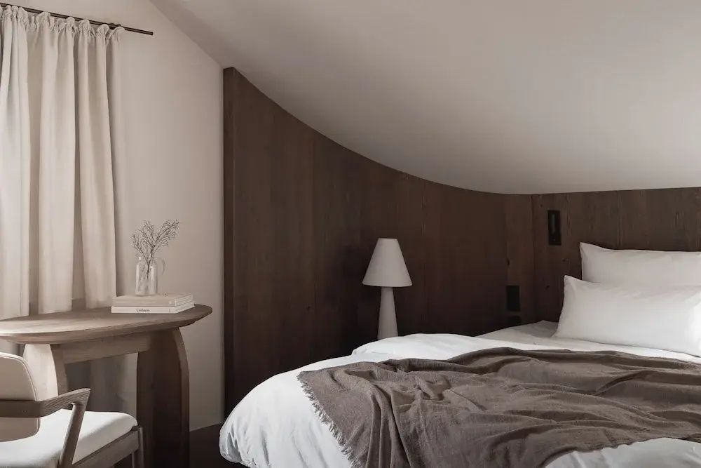 Schlafbereich mit Holzvertäfelung an der Wand, weißem Bett und brauner Tagesdecke unter einer Schräge.