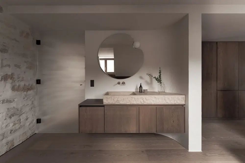 Modernes Badezimmer mit Waschtisch aus Holz und Stein sowie einem runden Spiegel an der Wand.