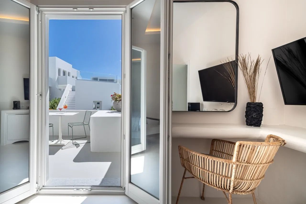 Blick aus dem Zimmer auf die Terrasse mit Sitzgelegenheiten und den blauen Himmel.