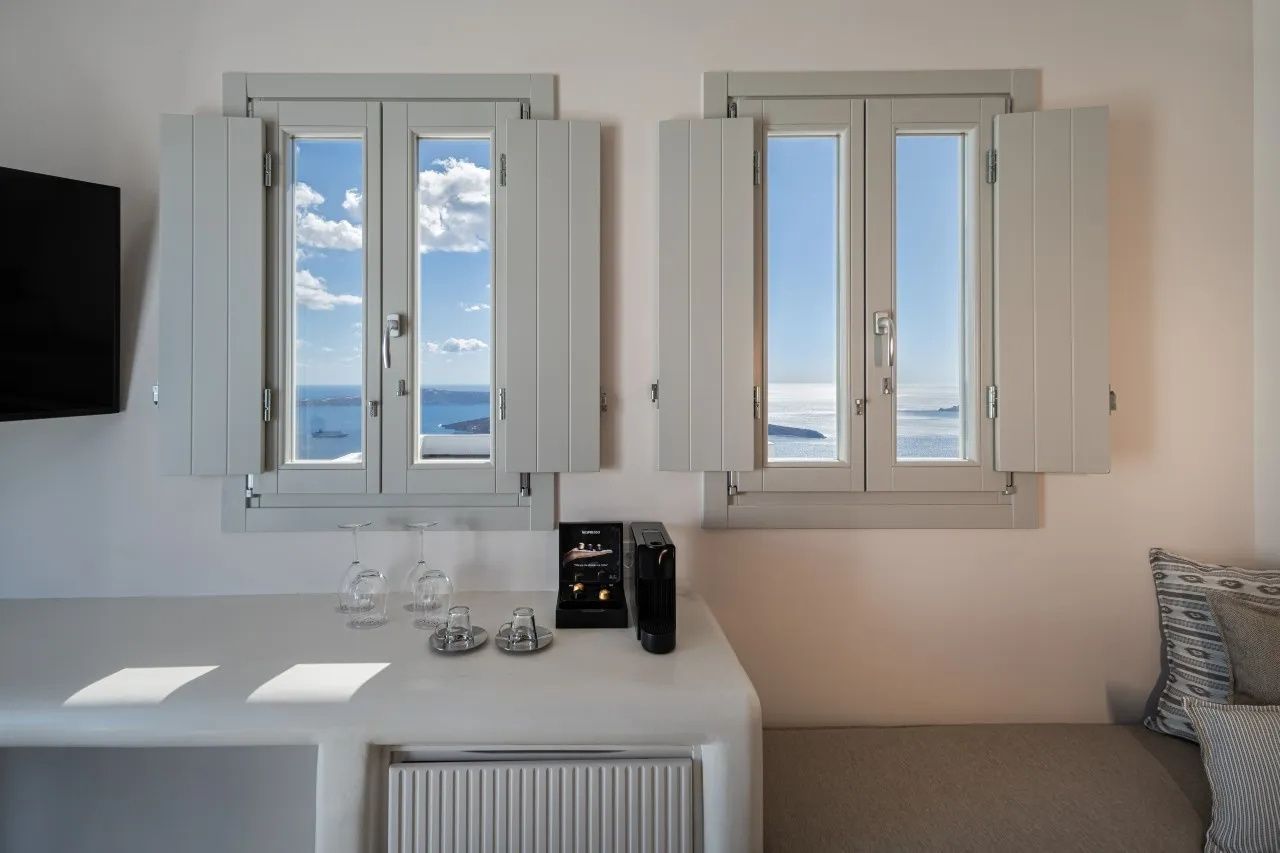 Blick durch zwei geöffnete Holzfenster auf das blaue Meer und die Caldera von Santorin.
