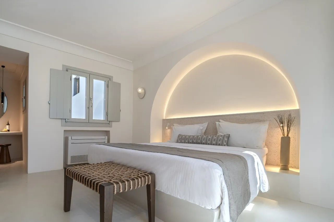 Doppelbett im hellen Hotelzimmer mit beleuchteter Wandnische und Fenster.