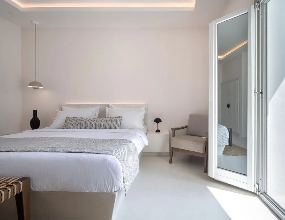 Modernes Schlafzimmer mit weißem Doppelbett, gemütlichem Sessel und einem großen Spiegel.