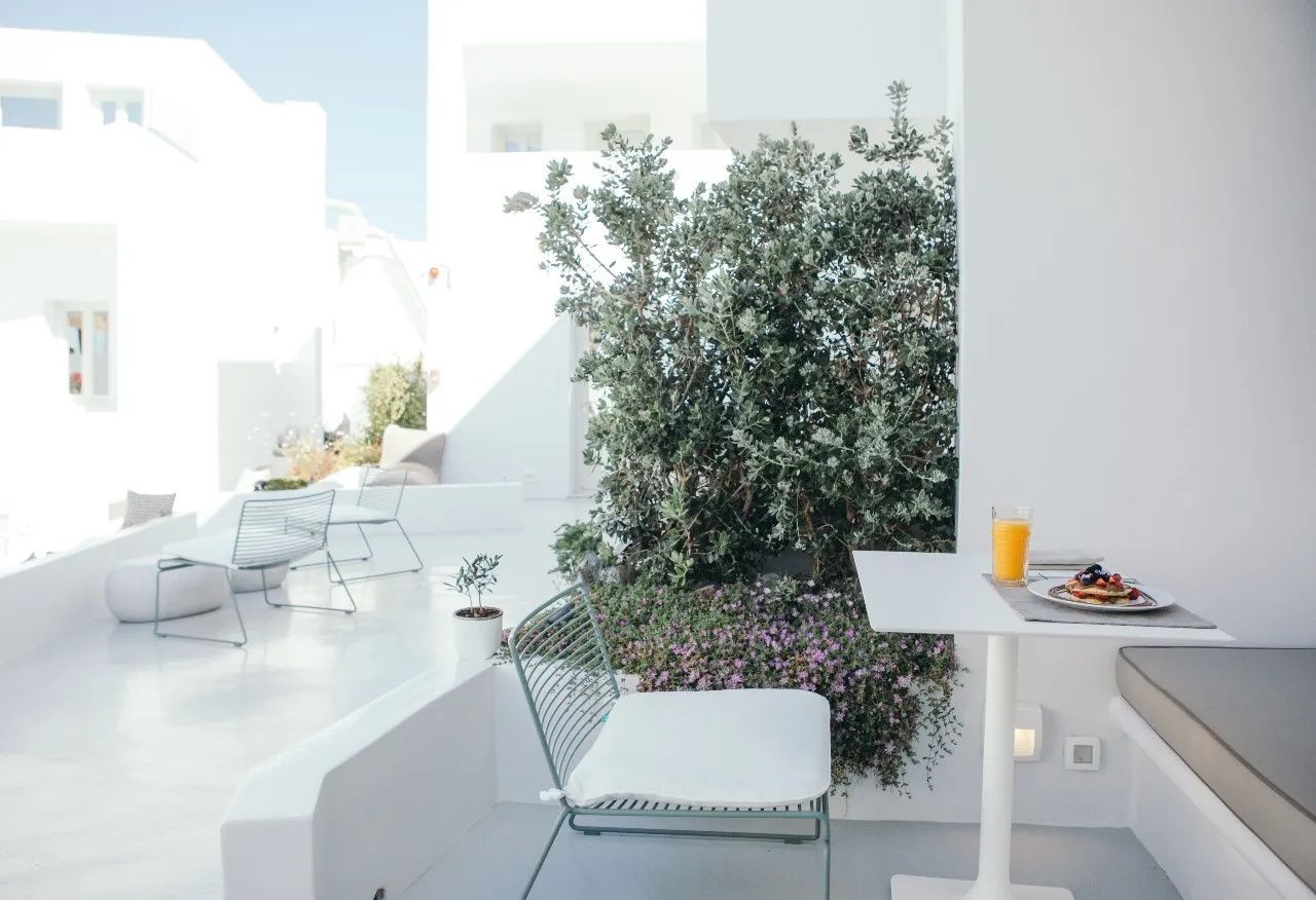 Weiße Terrasse mit Sitzgelegenheiten, bepflanzten Beeten und Blick auf die Hotelarchitektur.