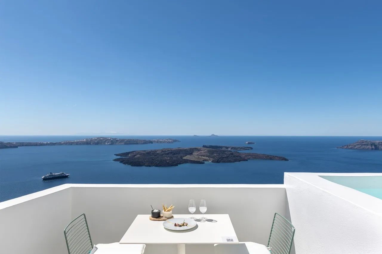 Gedeckter Tisch mit zwei Stühlen auf einer weiß getünchten Terrasse mit Blick über das blaue Meer.