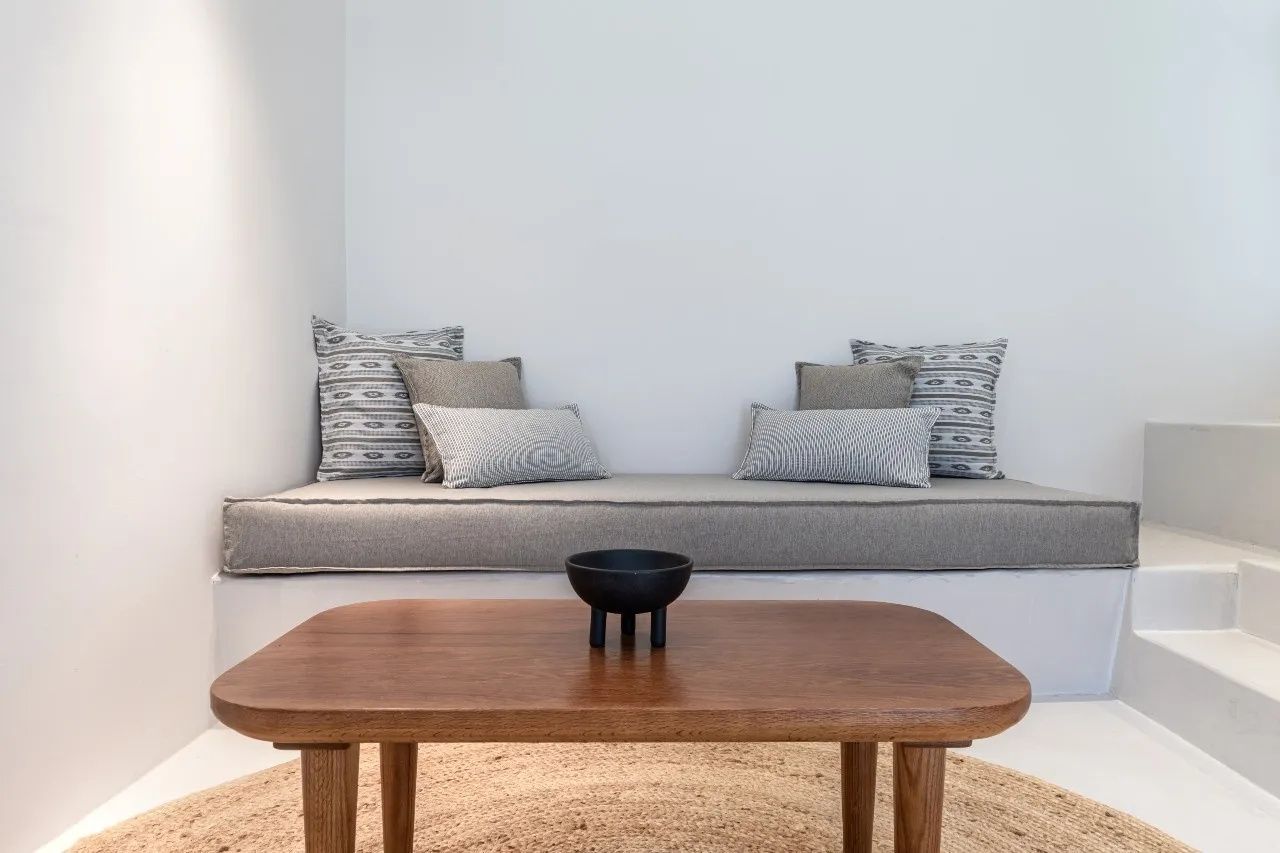Sitzecke mit gepolsterter Bank, verschiedenen Kissen, Holztisch und rundem Teppich.
