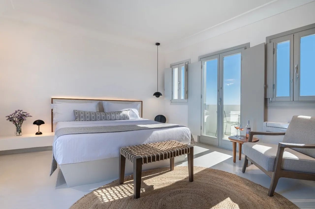 Helles Hotelzimmer mit Doppelbett, Teppich, Sitzbank und Blick durch die Balkontür.