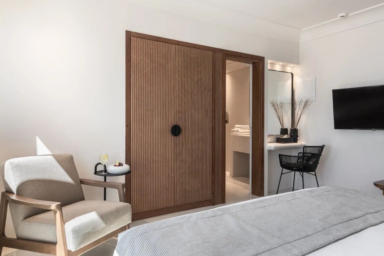 Schlafbereich mit Holzschrank, Blick ins Badezimmer und einem Schminktisch mit Spiegel und Stuhl.