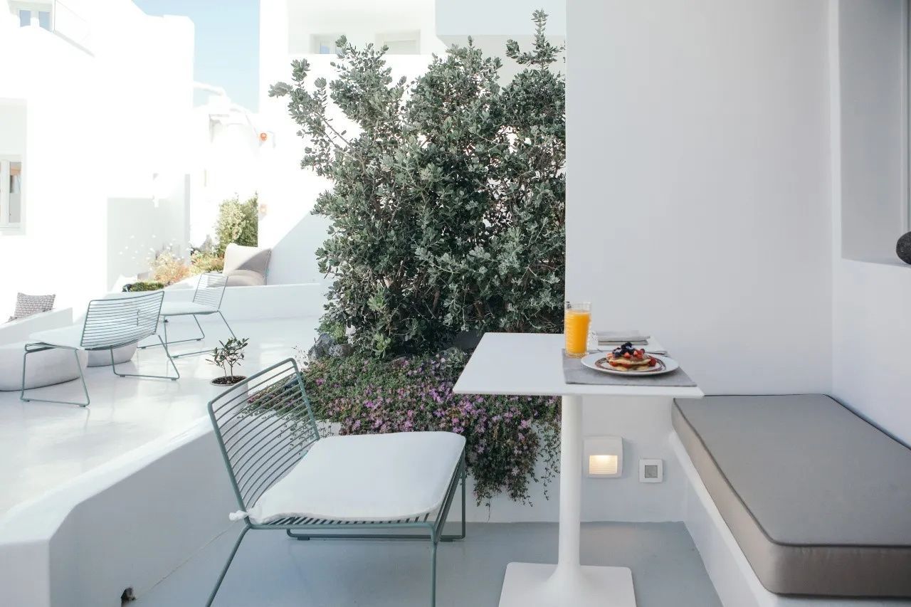 Sonnige Terrasse mit einem Tisch, Frühstück und Stuhl neben grünen Sträuchern.