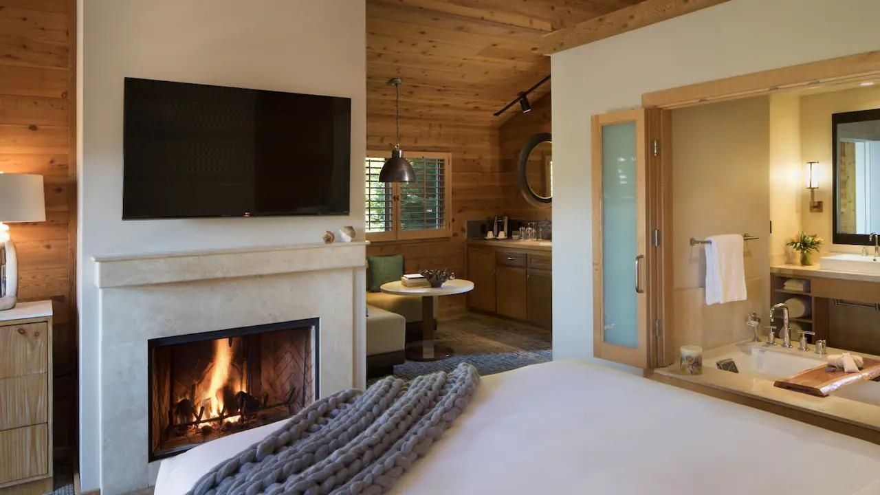 Hotelzimmer mit brennendem Kamin, Holzdecke, Bett im Vordergrund und Sitzecke im Hintergrund.