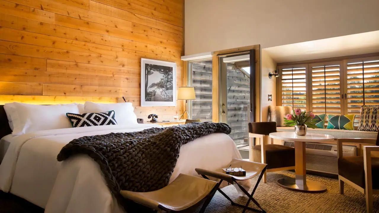 Hotelzimmer mit großem Bett, Holzwand, zwei Hockern am Fußende und Schreibtisch.