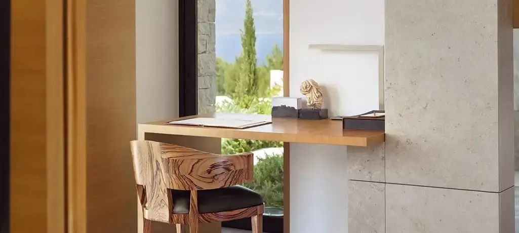 Holzschreibtisch mit Holzstuhl vor einem Fenster mit Blick auf grüne Zypressen.