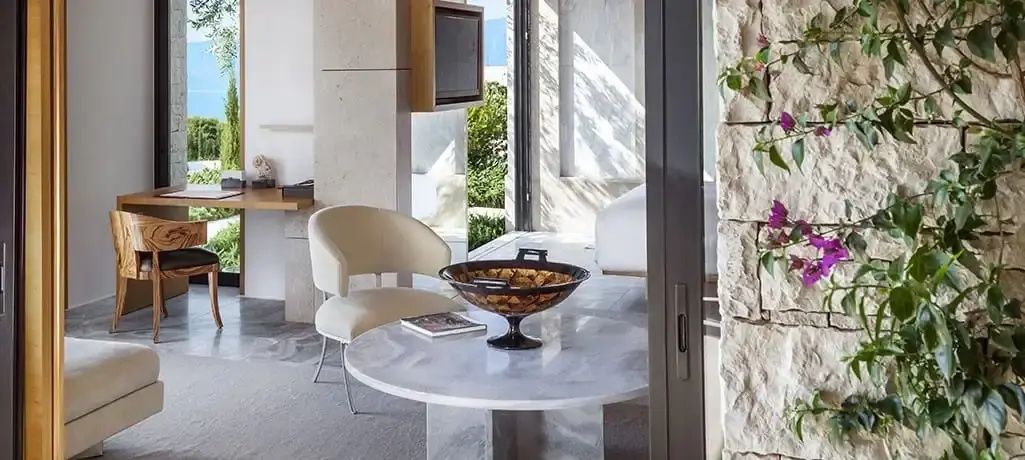 Runder Marmortisch mit Schale und hellem Sessel im Wohnbereich einer Suite.