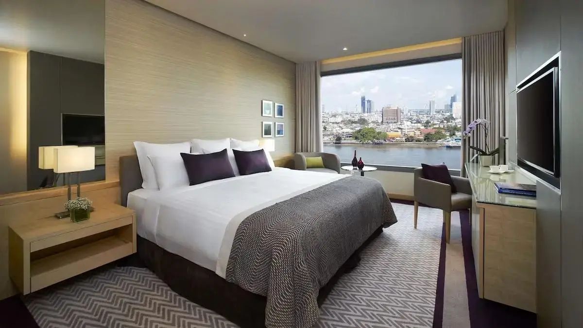 Doppelbett im hellen Hotelzimmer mit breiter Fensterfront und Blick auf den Fluss