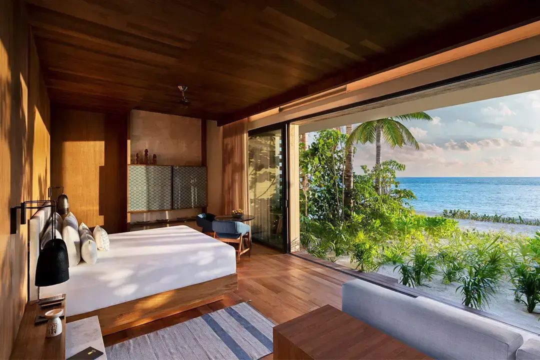 Schlafzimmer mit Holzdecke, Doppelbett und geöffneter Glasfront zum Strand und Meer.