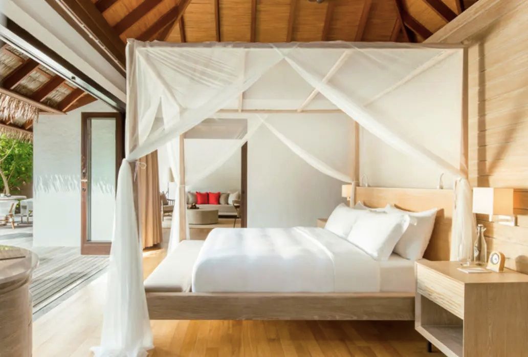 Helles Schlafzimmer einer Villa mit Holzfußboden und einem großen Himmelbett mit weißem Moskitonetz.