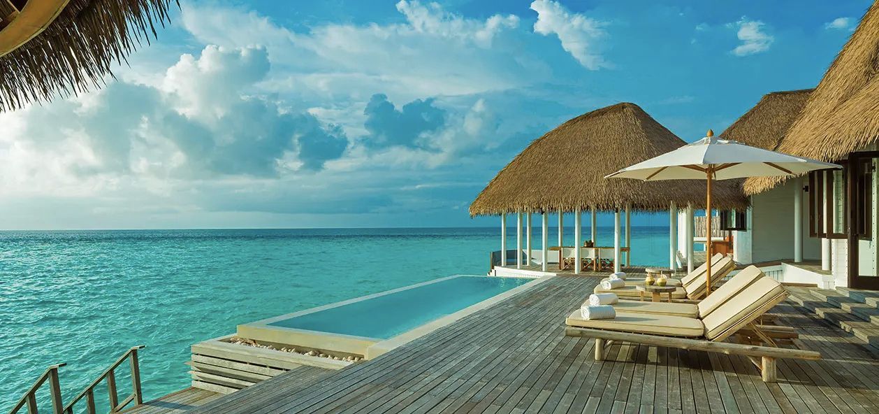 Rechteckiger Pool auf einer Holzterrasse direkt über dem Meereswasser neben einem Pavillon.