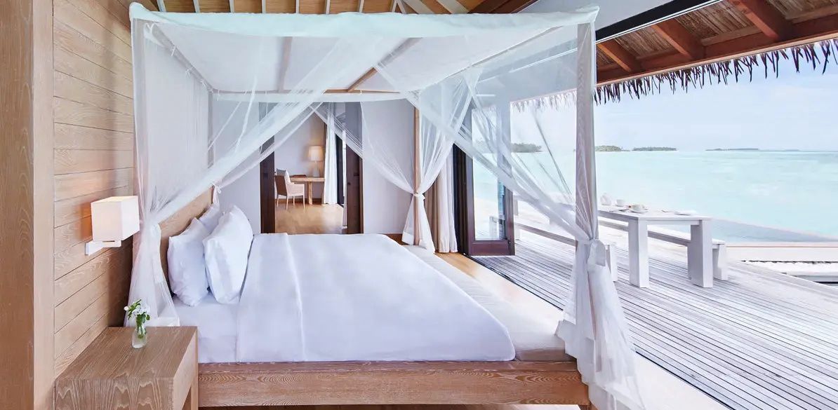 Himmelbett mit weißem Moskitonetz im Schlafbereich einer Wasservilla mit Blick aufs Meer.