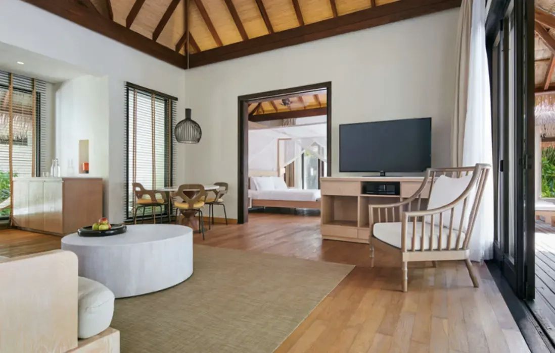 Wohnbereich einer Villa mit Fernseher, Sesseln, Esstisch und Blick auf ein angrenzendes Schlafzimmer.