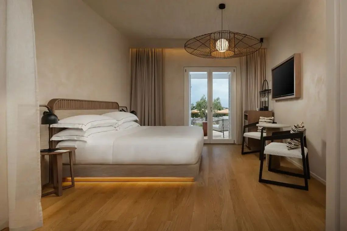 Doppelbett im Hotelzimmer mit Holzboden und Balkontür ins Freie.