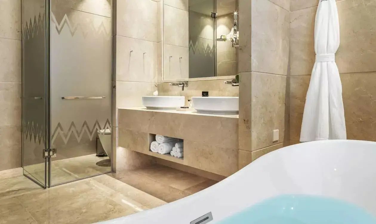 Modernes Badezimmer aus hellen Natursteinfliesen mit Doppelwaschbecken und Spiegel.