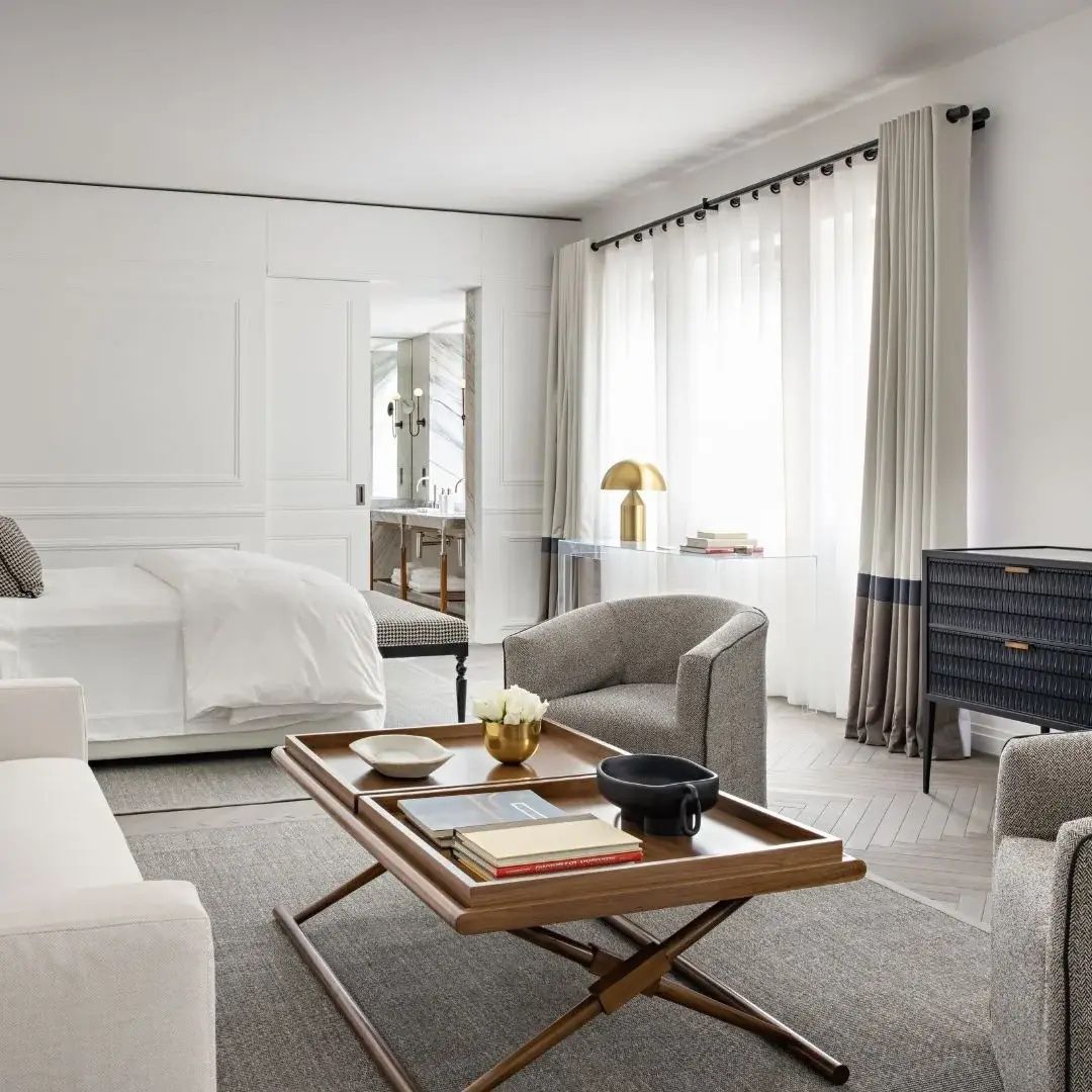 Wohnbereich im Hotelzimmer mit Holztisch, Sesseln und bodentiefem Fenster.
