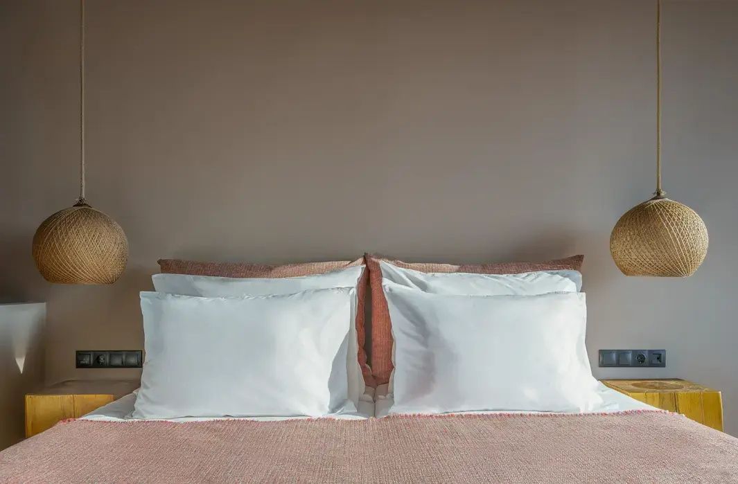 Doppelbett mit weißen Kopfkissen und erdfarbener Wand im Hotelzimmer.
