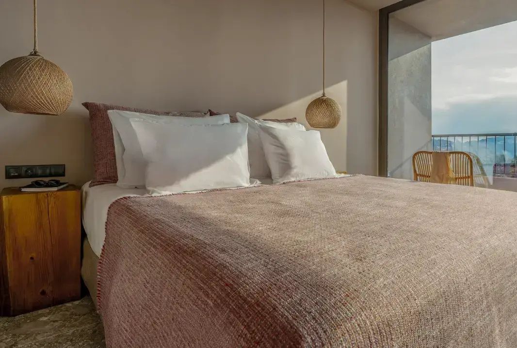 Doppelbett mit roséfarbener Tagesdecke und Kissen im Hotelzimmer.