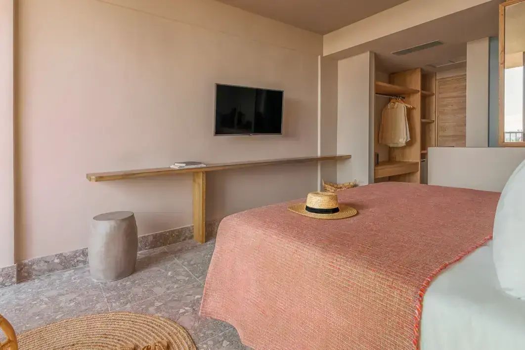 Modernes Hotelzimmer mit Flachbildfernseher, Holzelementen und Strohhut auf dem Bett.