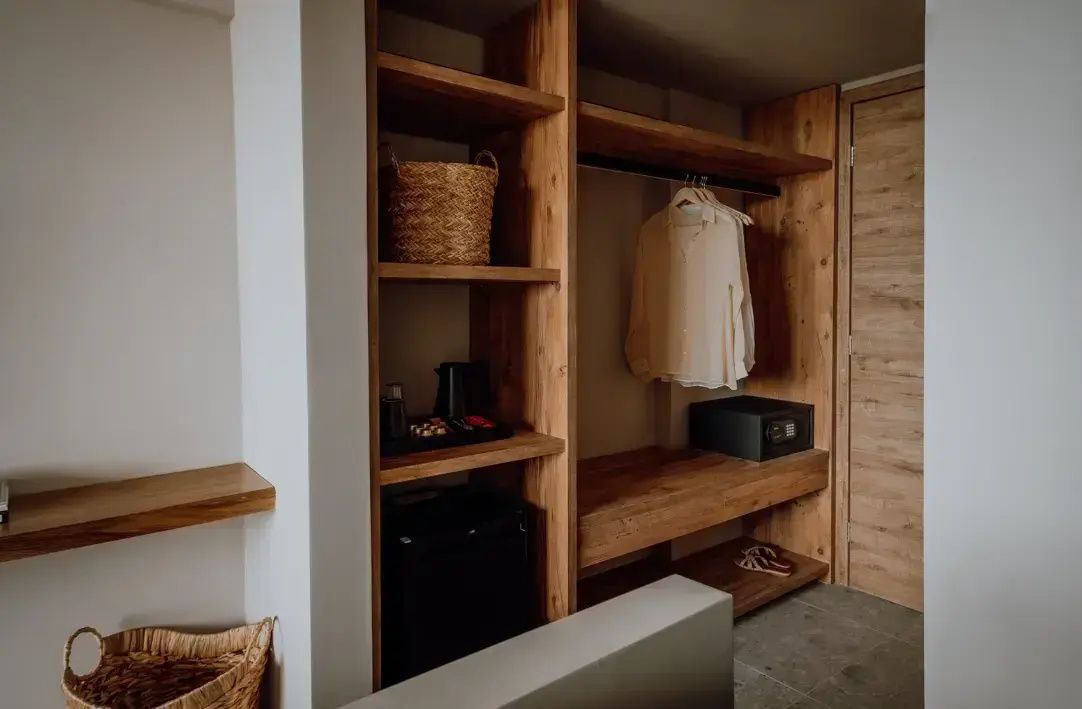 Offener Kleiderschrank aus Holz mit Minibar, Safe, Regalen und geflochtenem Korbelement.