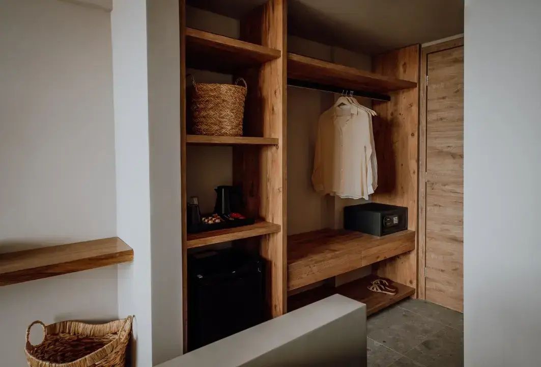 Offenes Holzregal im Hotelzimmer mit Minibar, Safe, Kleiderstange und Korb.