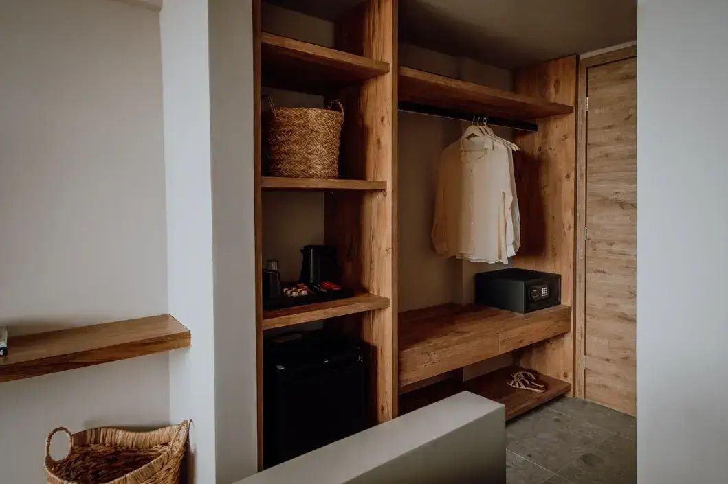 Offener Kleiderschrank aus Holz mit Safe, Minibar und Ablageflächen im Zimmer.