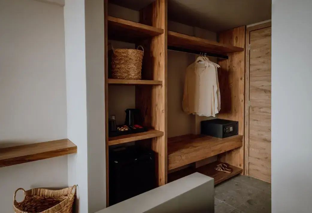 Offener Kleiderschrank aus Holz mit Regalen, Safe und Minibar im Hotelzimmer.