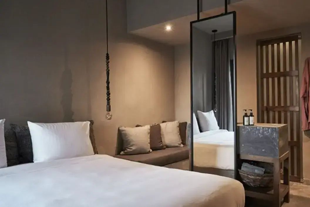 Modernes Hotelzimmer mit weiß bezogenem Bett, Sitzbank und großem Spiegel.