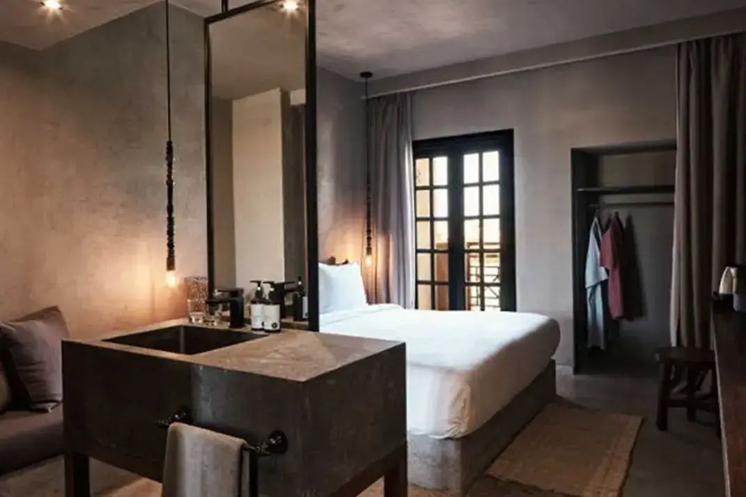 Modern eingerichtetes Hotelzimmer mit Doppelbett, Waschtisch aus Beton und großer Fenstertür.