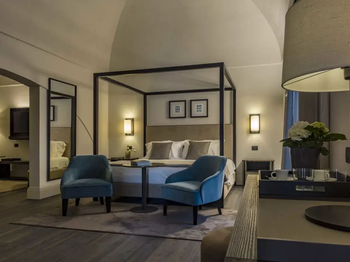 Hotelzimmer mit Gewölbedecke, Baldachinbett, zwei blauen Sesseln und einem Beistelltisch.