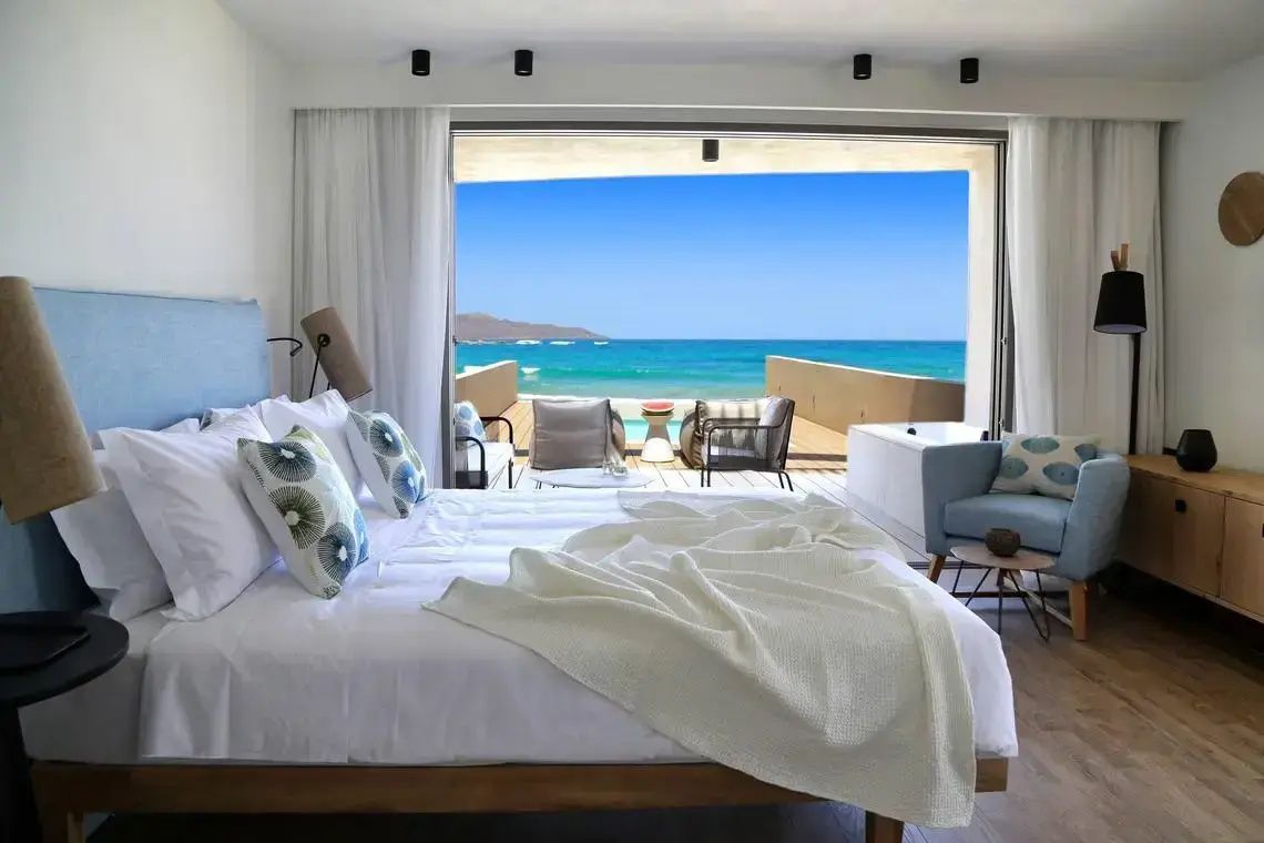 Blick aus dem Hotelzimmer über eine Terrasse mit Pool auf das blaue Meer und den Strand.