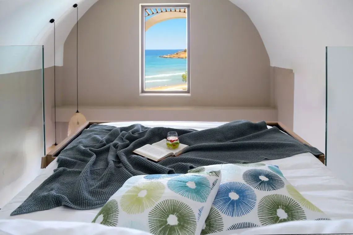 Bett mit grauer Decke und Kissen unter einer gewölbten Decke mit Blick auf das Meer.