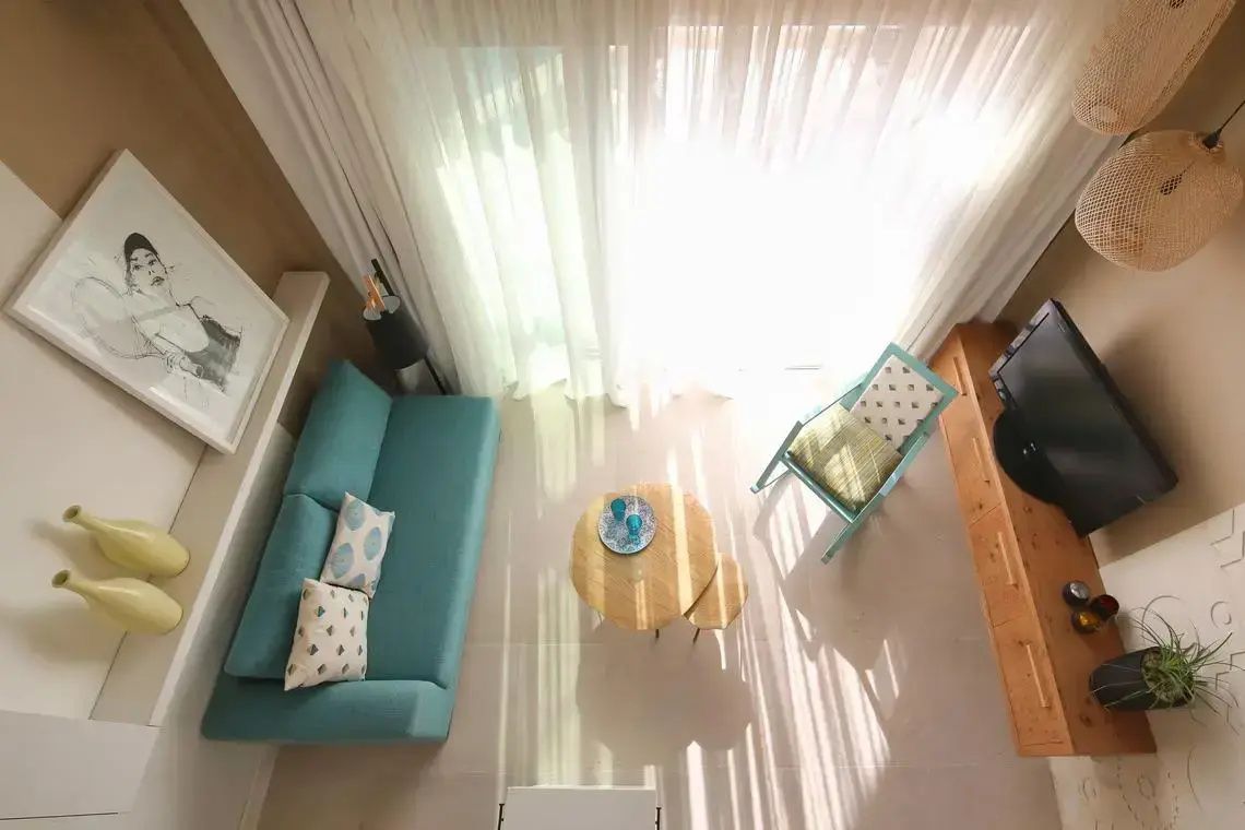 Vogelperspektive auf einen hellen Wohnbereich mit türkisem Sofa und hölzernem Couchtisch.