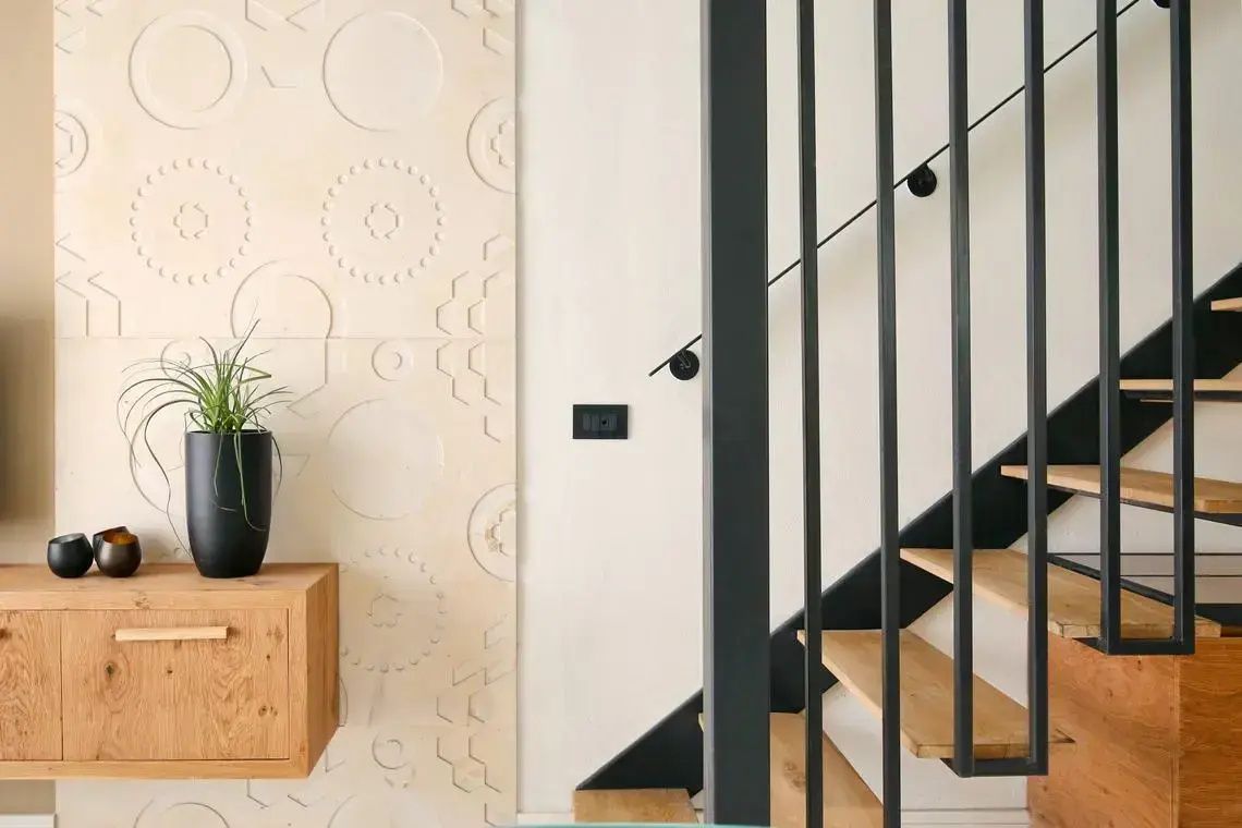 Holztreppe mit schwarzem Geländer neben einer strukturierten Wand im Innenbereich.